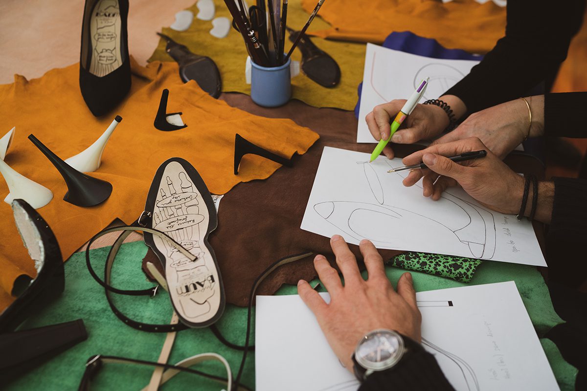 Hands drawing on pieces of paper in a workshop setting with shoe insoles