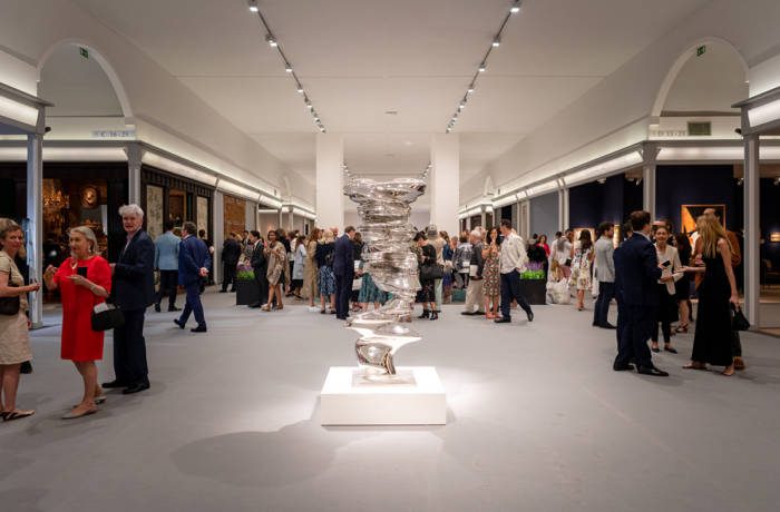 Installation shot of an art fair with guests walking around a sculpture