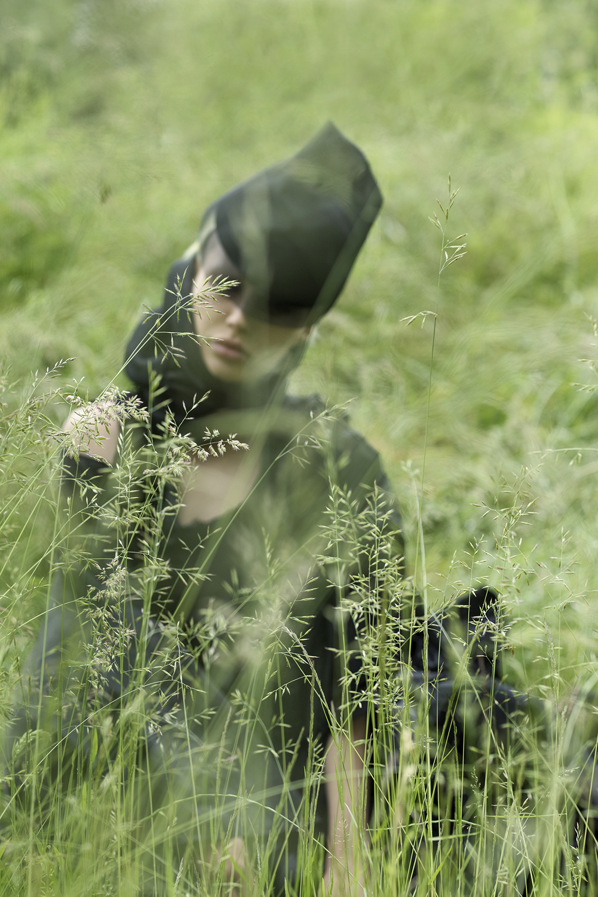 Model half hidden in long grass wearing black clothing