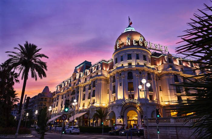 Facade of a hotel at night lit with a purple sunset behind