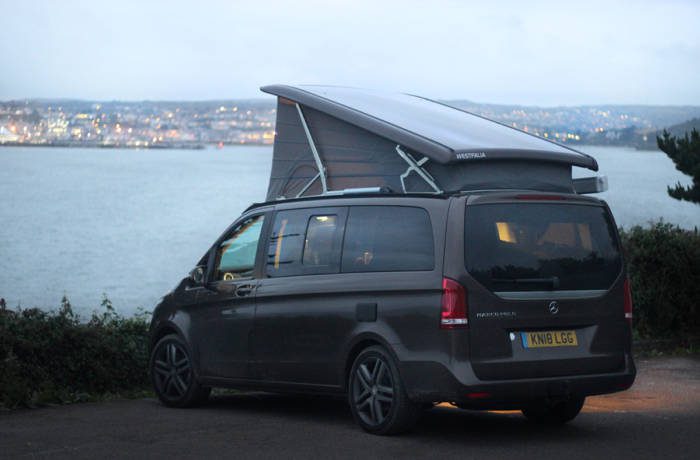 luxurious camper van with pop up roof and ocean in distance