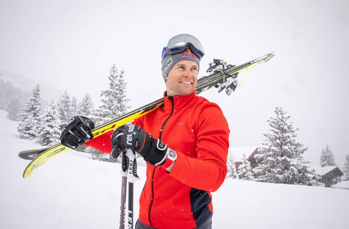 Man on ski slope wearing a red fleece with skis on his shoulder