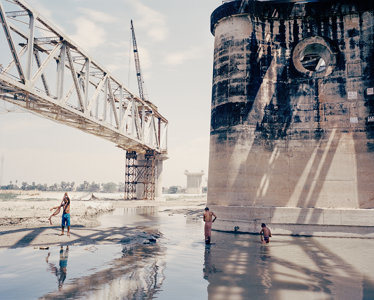 Industrial scene of men washing in water beneath a bridge