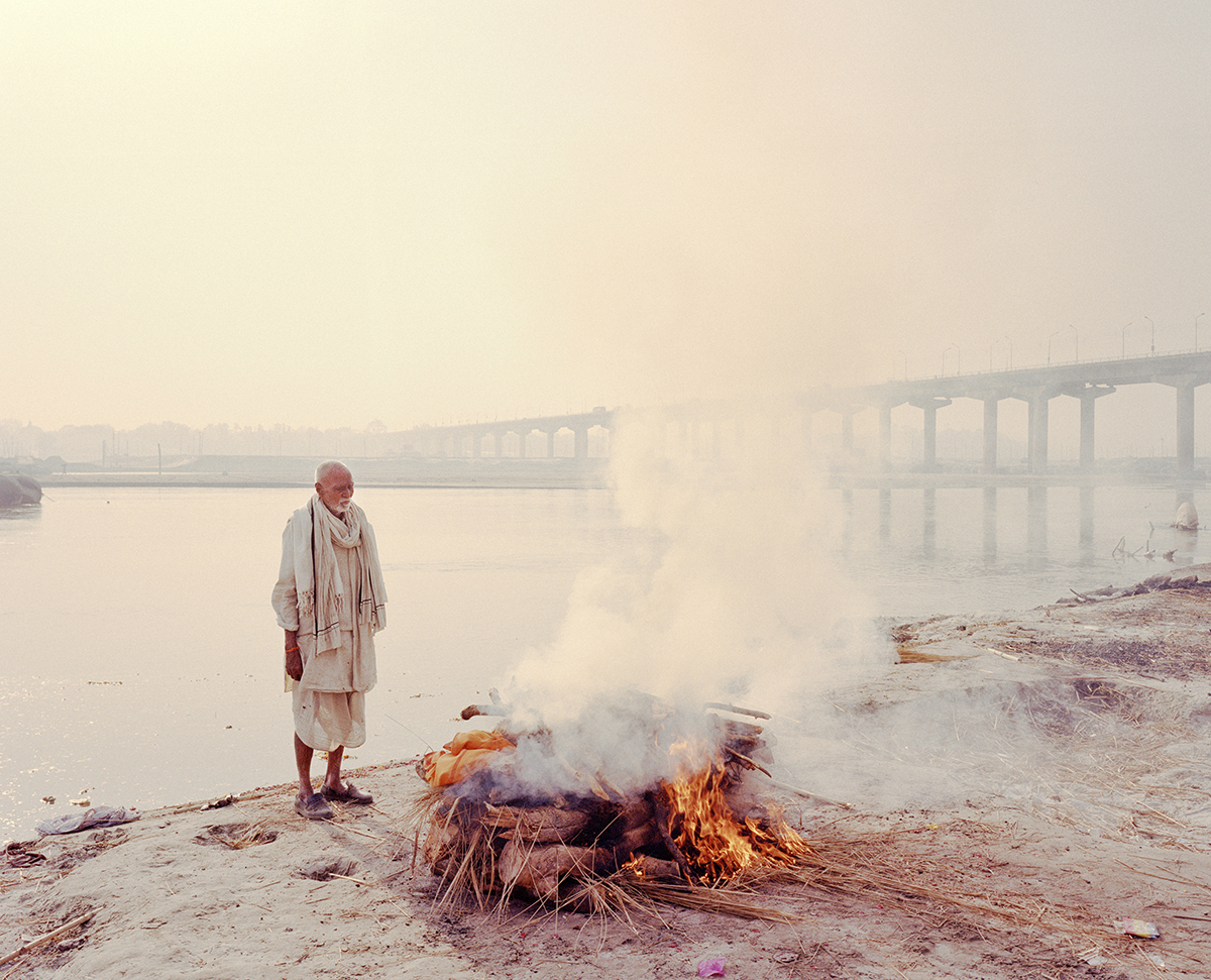 Photograph of man standing by funeral pyre on the riverside