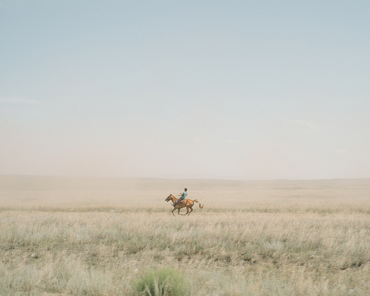 Photograph of a man riding a horse through empty wilderness
