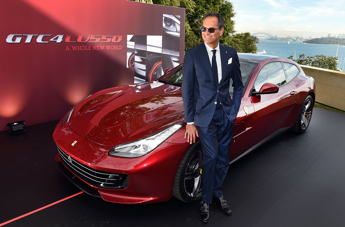 Man in a suit standing next to a red ferrari sportscar