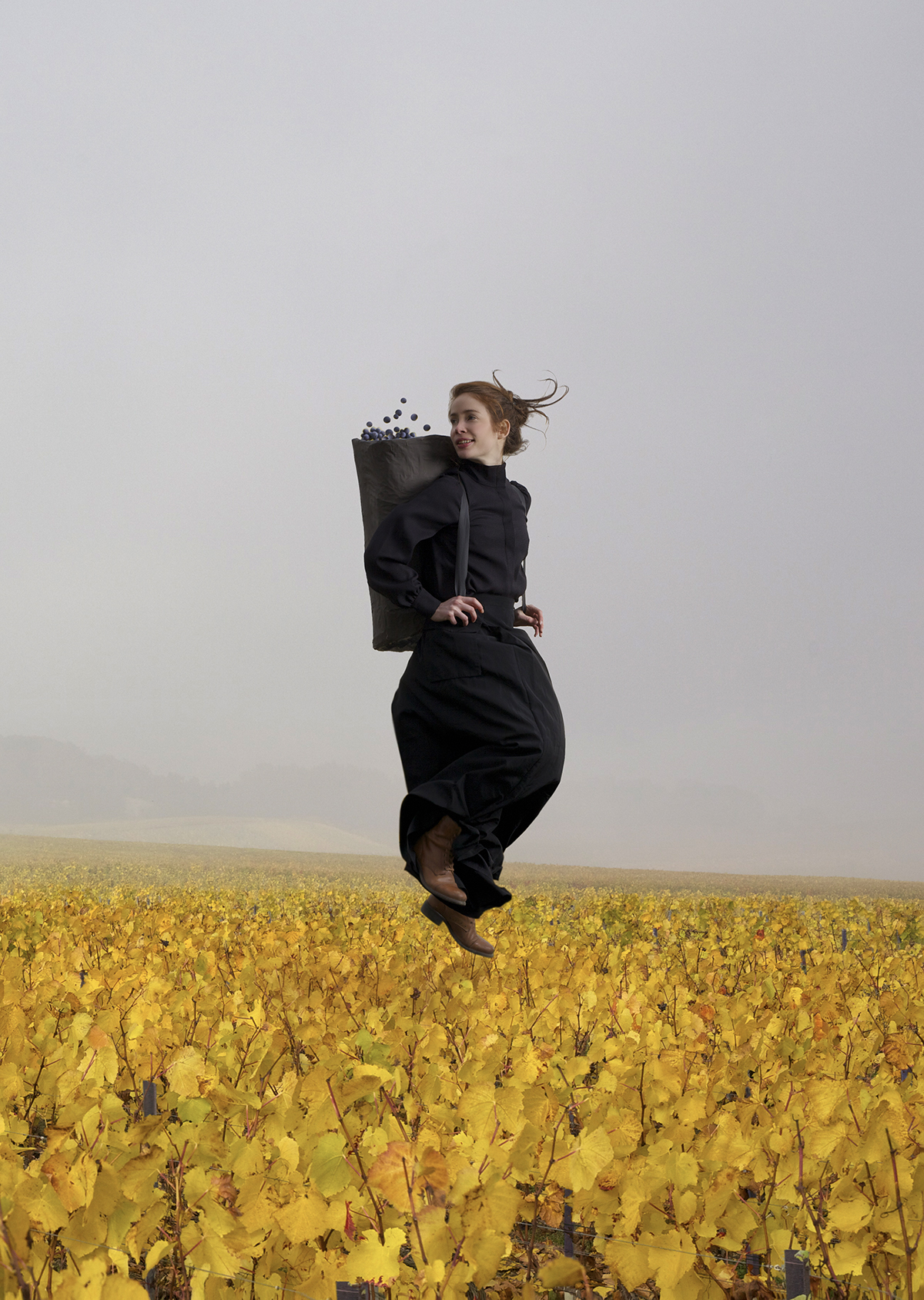 A woman jumping in a vineyard with a basket full of grapes