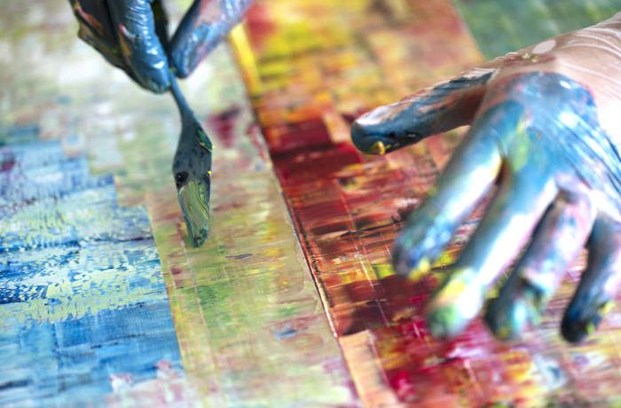 Painter's hands using a scraper to shave paint on a canvas