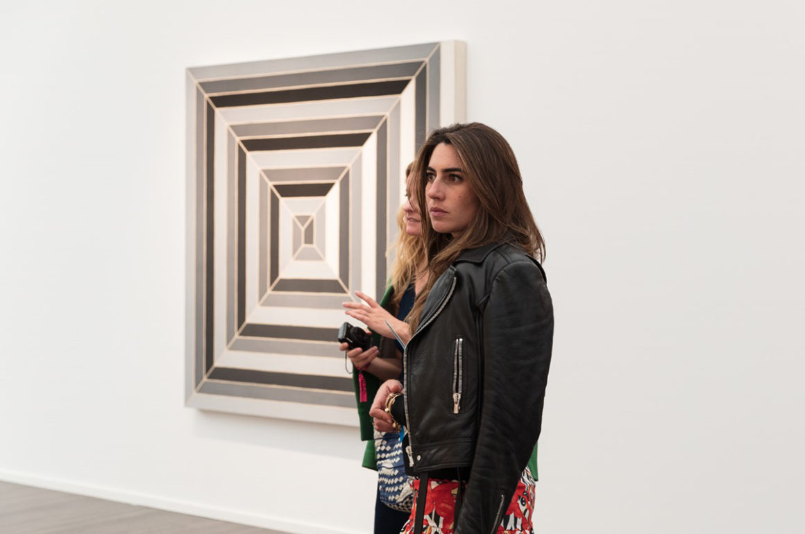 two woman standing in front of an abstract artwork at an exhibition