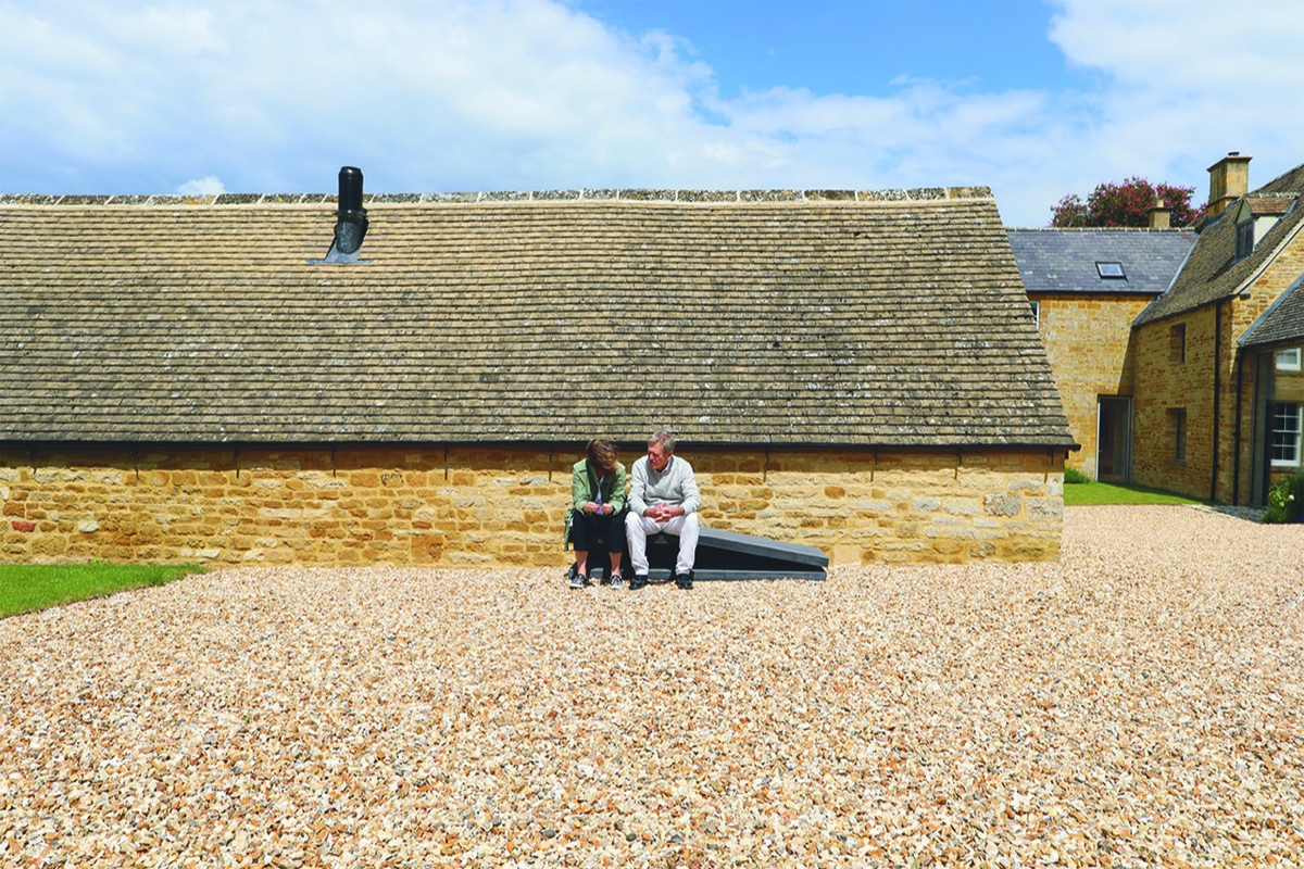 Ma and woman sitting on bench in gravel courtyard