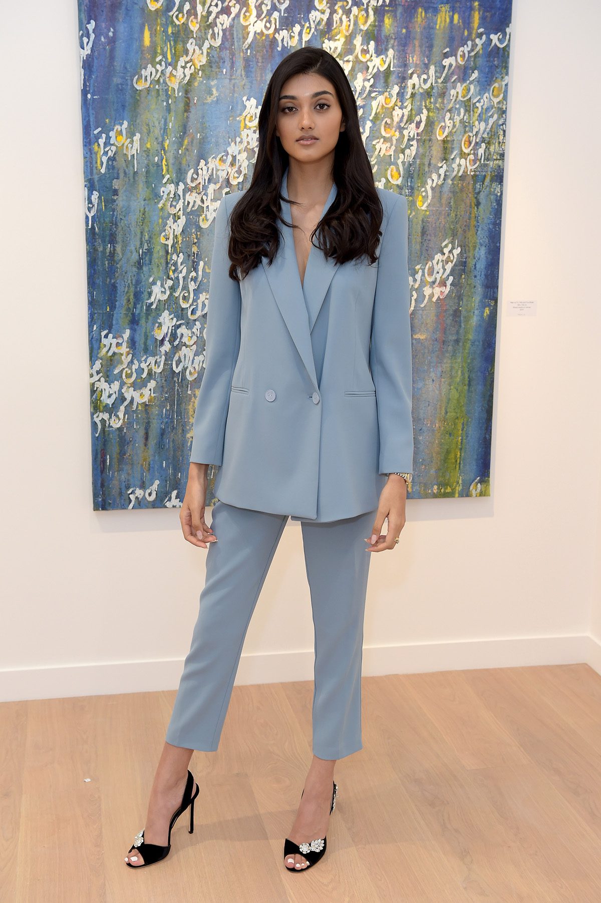 Woman in pale blue suit stands in front of painting