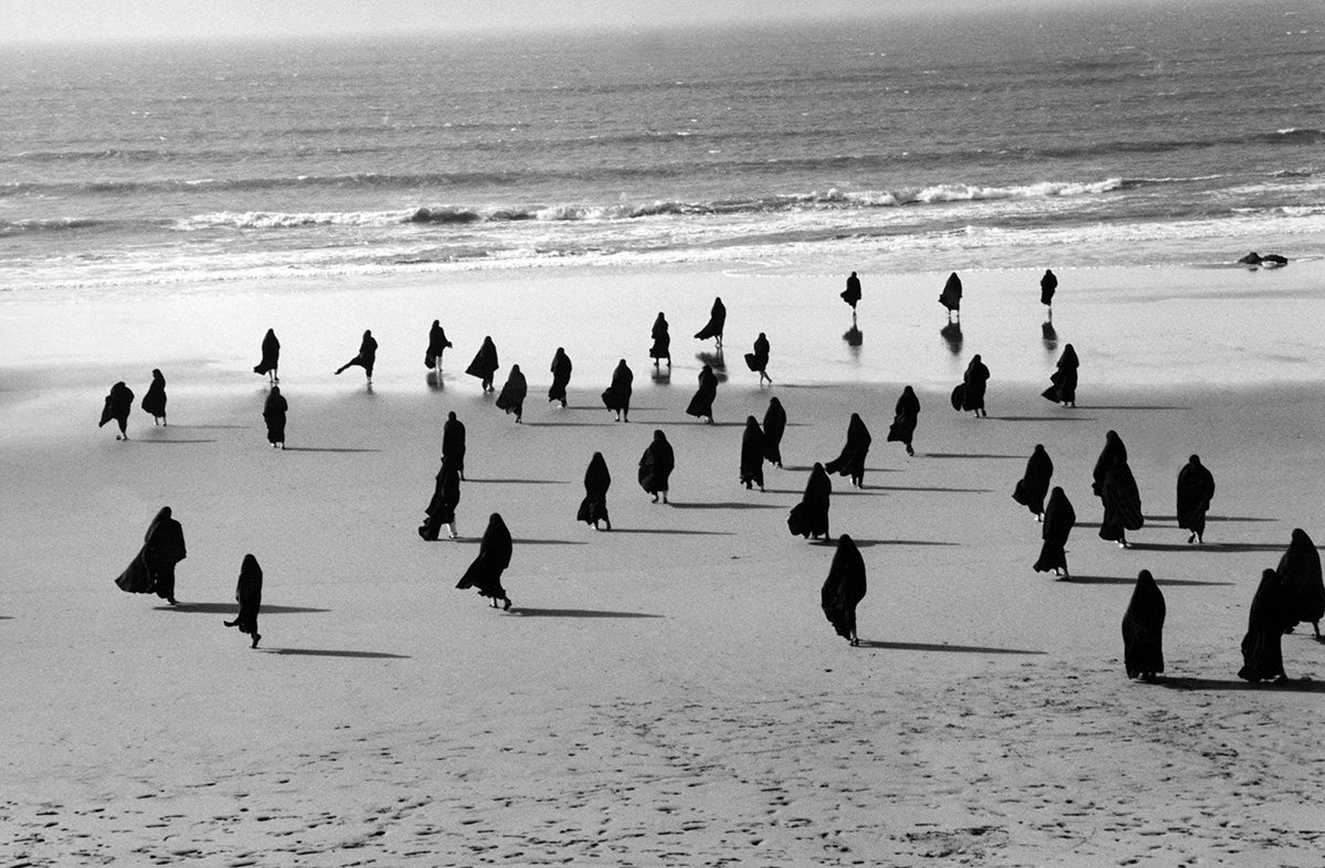 Veiled women walking across a beach towards the sea