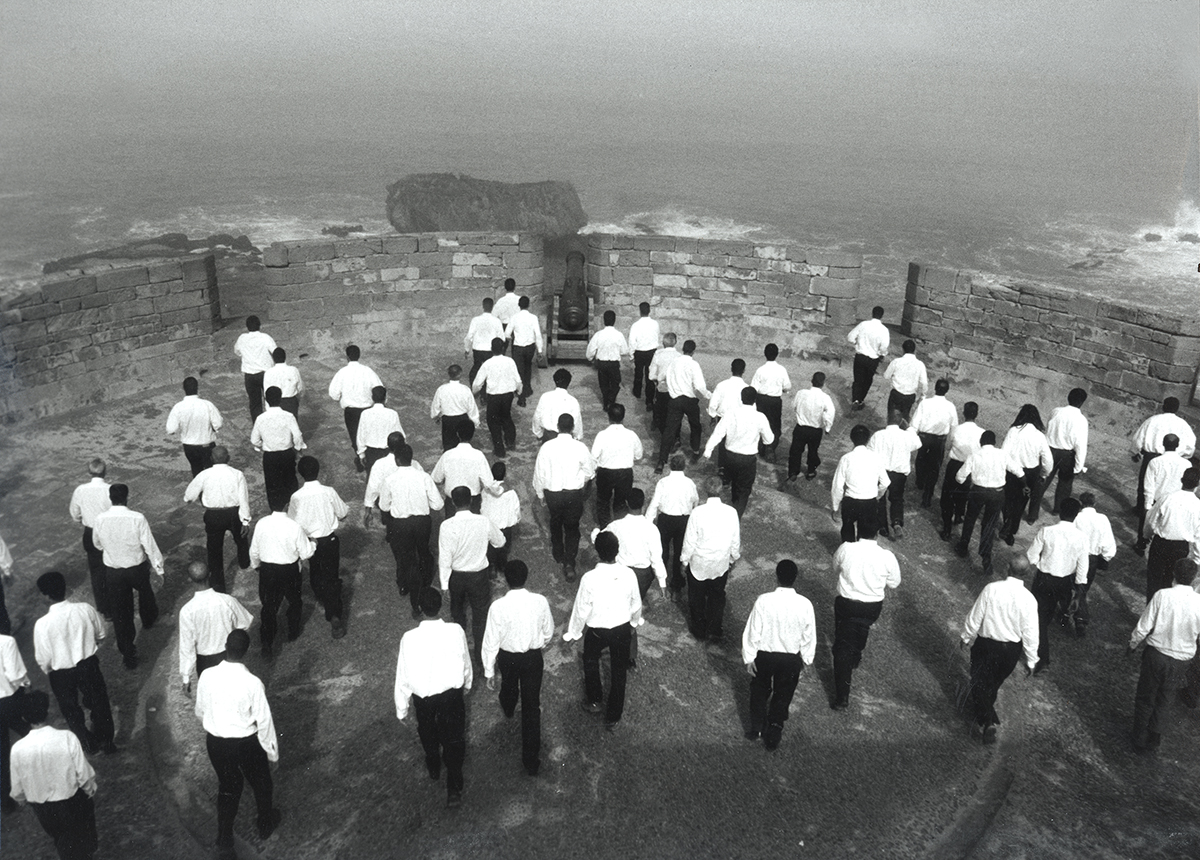 Monochrome image of white-shirted men on a cliff edge