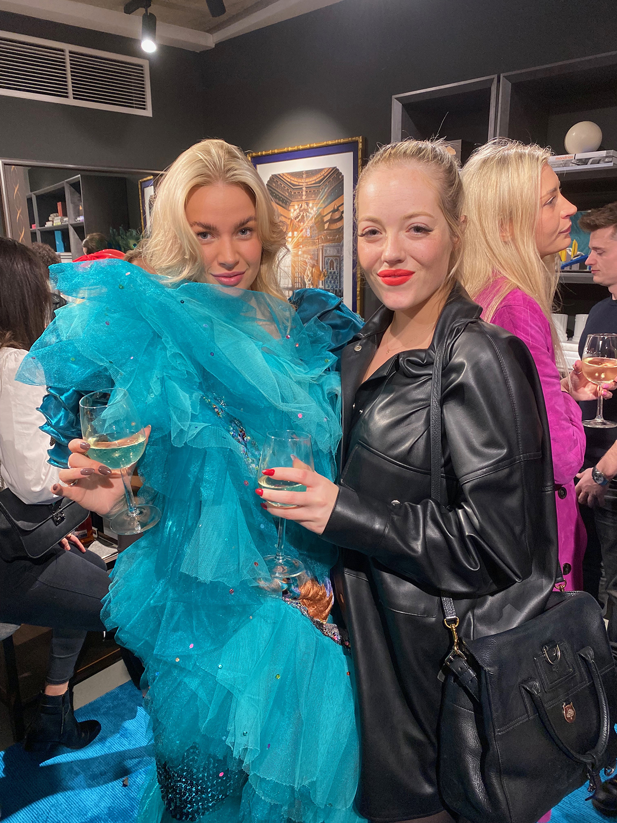 A woman in Turquoise feather dress next to a woman in a black leather coat