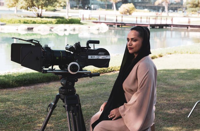 Nayla Al Khaja sitting by a film camera wearing a pink dress