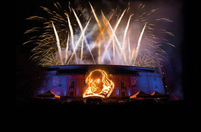 Fireworks and lights with William's Shakespeare's face on the side of a theatre