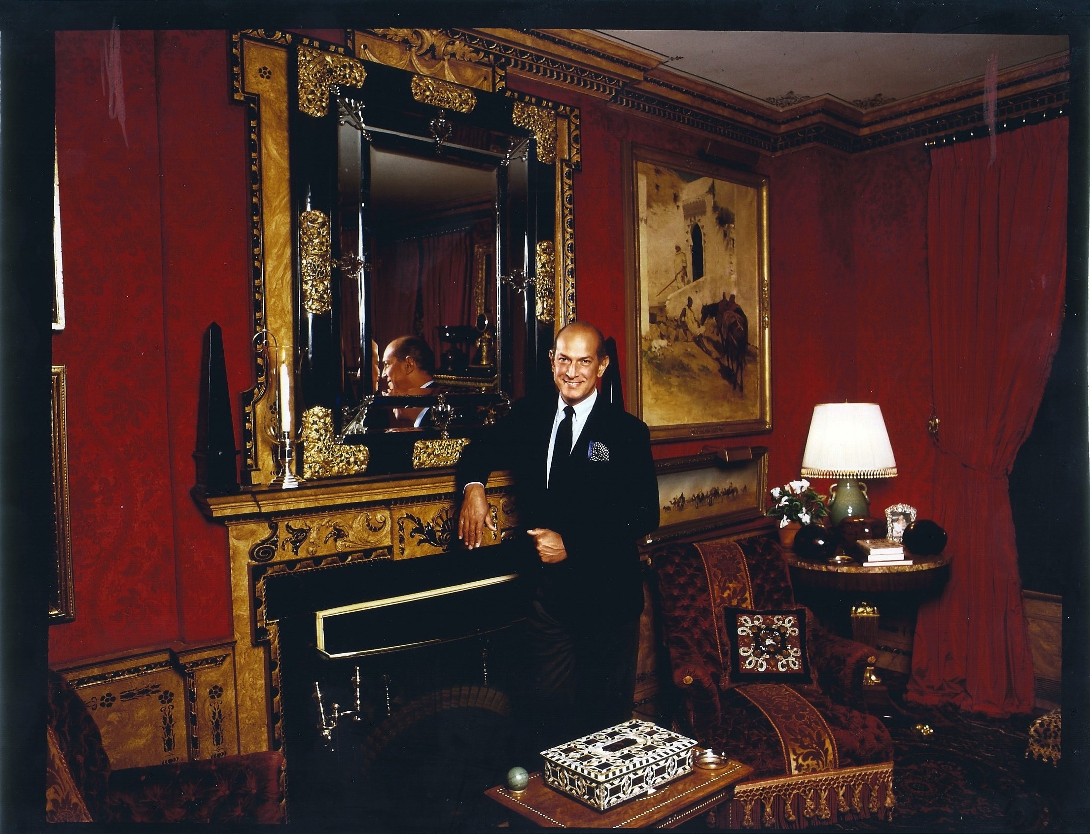 Oscar de la Renta standing in a red room by a mirror