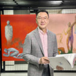 Patrick Sun holding an open book standing in front of a painting