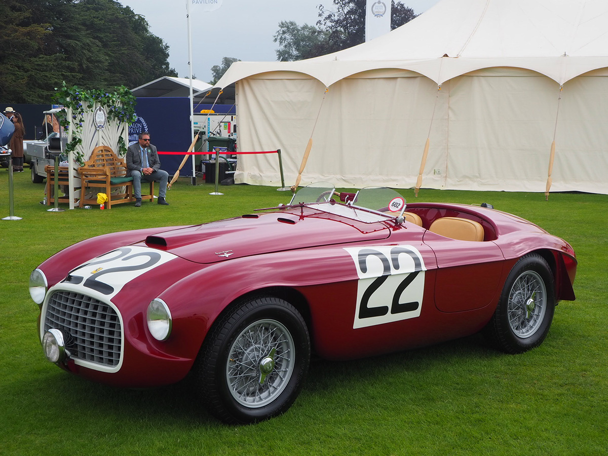 an old red Ferrari parked in front of a white tent on the grass