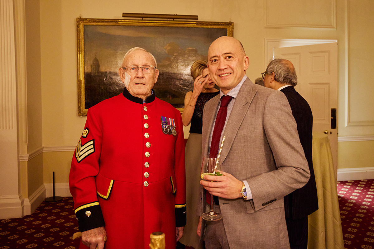 An old man in a red army uniform standing next to a man in a suit