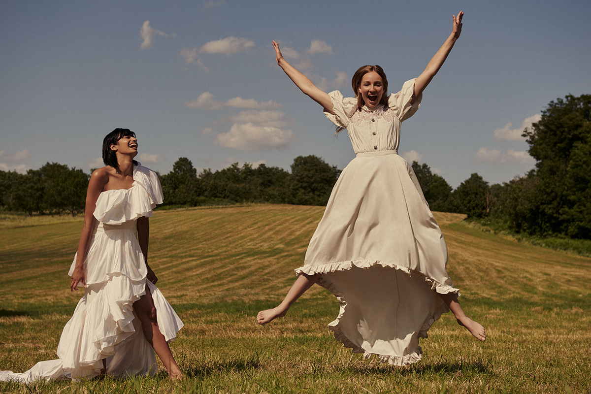 Two girls jumping in a field in white dresses