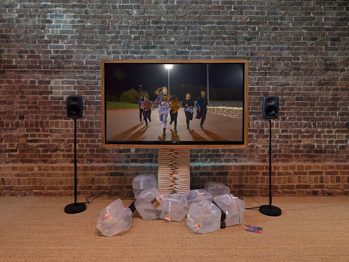 A tv screen in front of a brick wall with bin bags on the floor and people on the screen