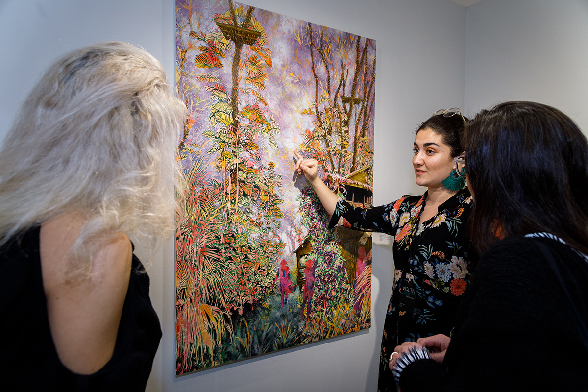 A woman showing people an art work of flowers painted on a canvas
