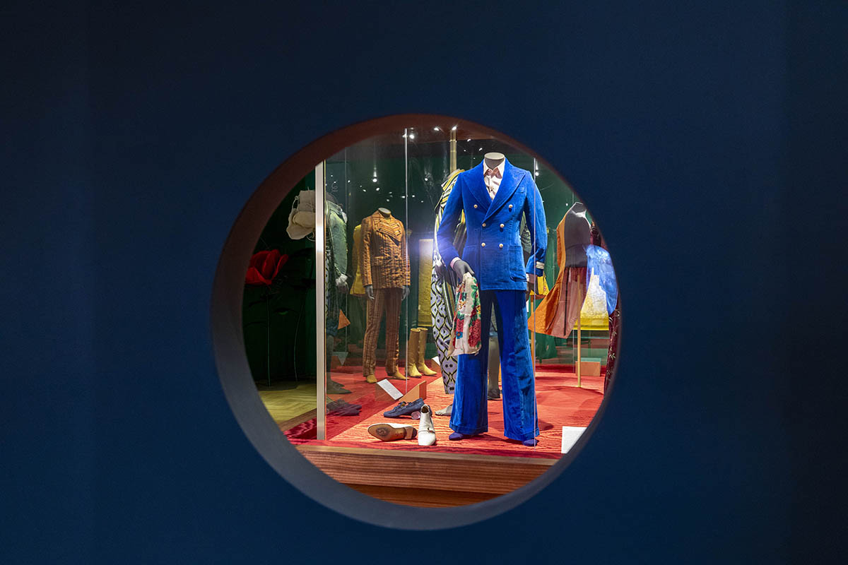 A blue suit shown at an exhibition through a hole in a blue wall