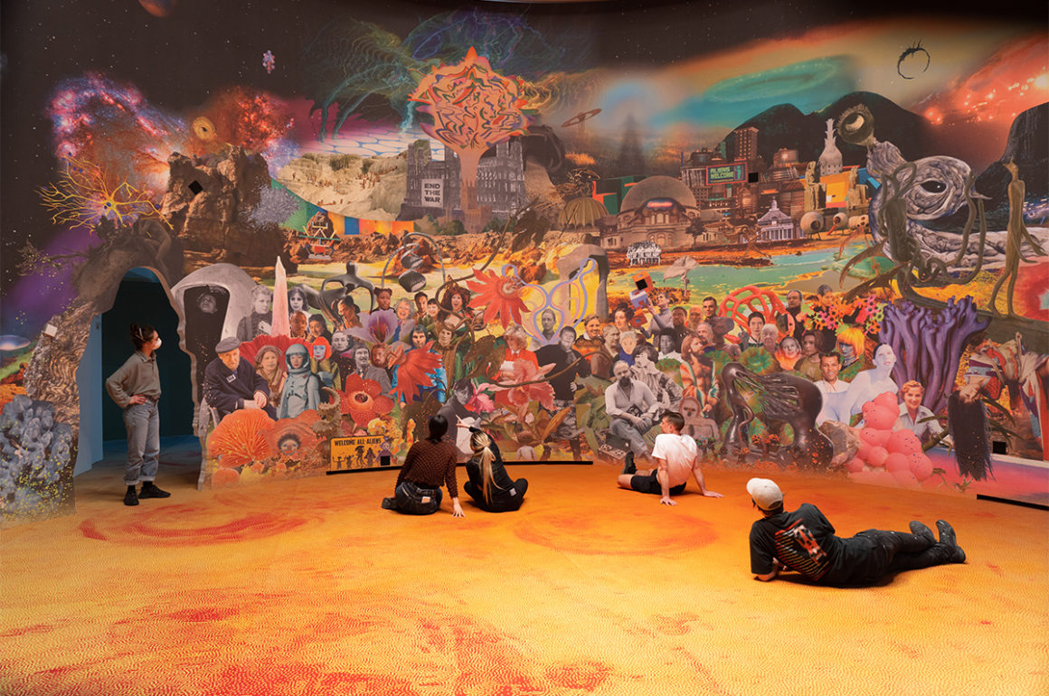people sitting on an orange floor in front of a mural of a village