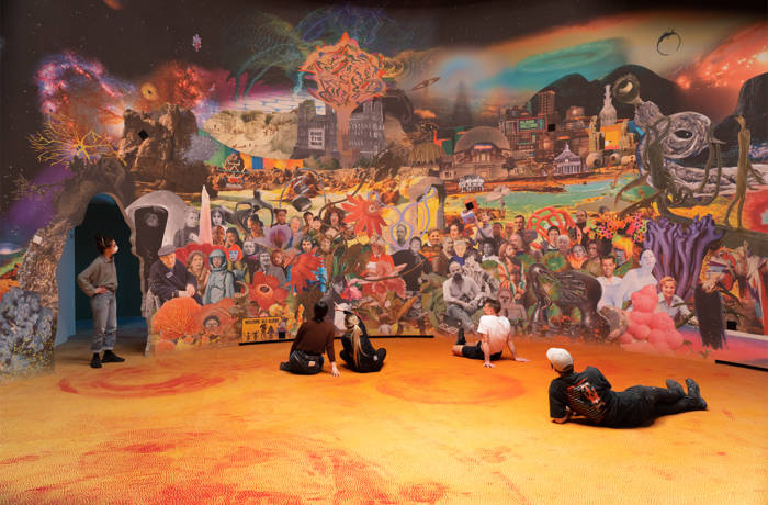 people sitting on an orange floor in front of a mural of a village