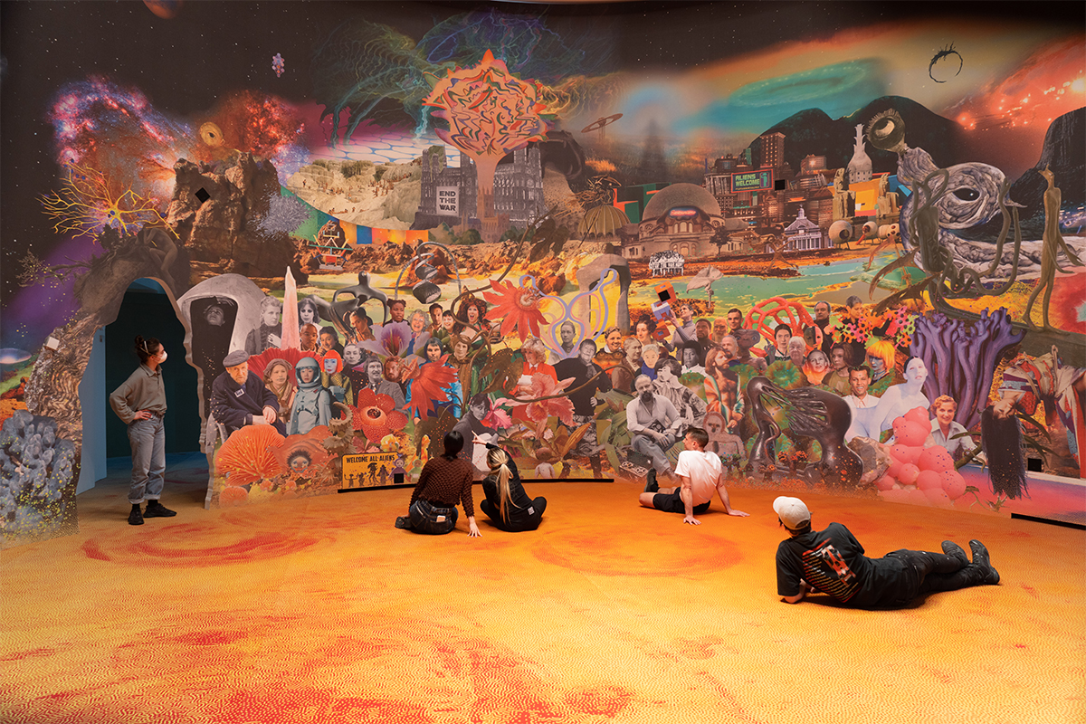 people sitting on an orange floor in front of a mural of a village 