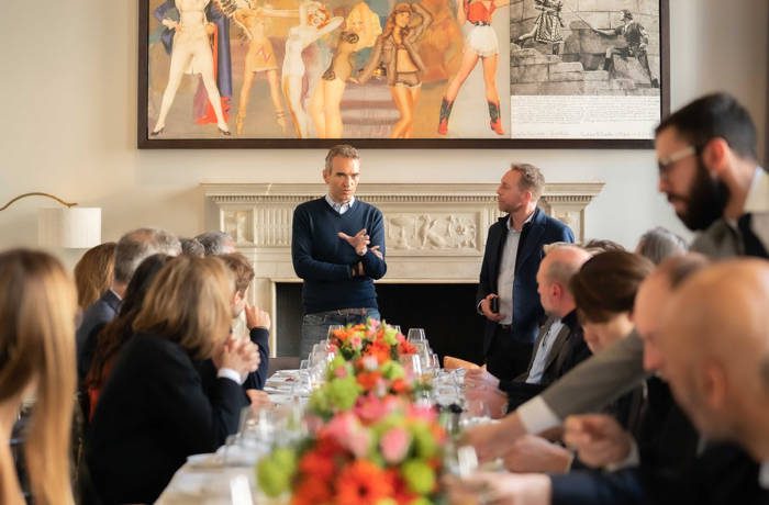 two men standing at the end of a table giving a talk