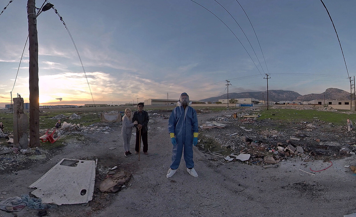 A man in a blue jumpsuit and mask standing on a road with a man and woman behind him
