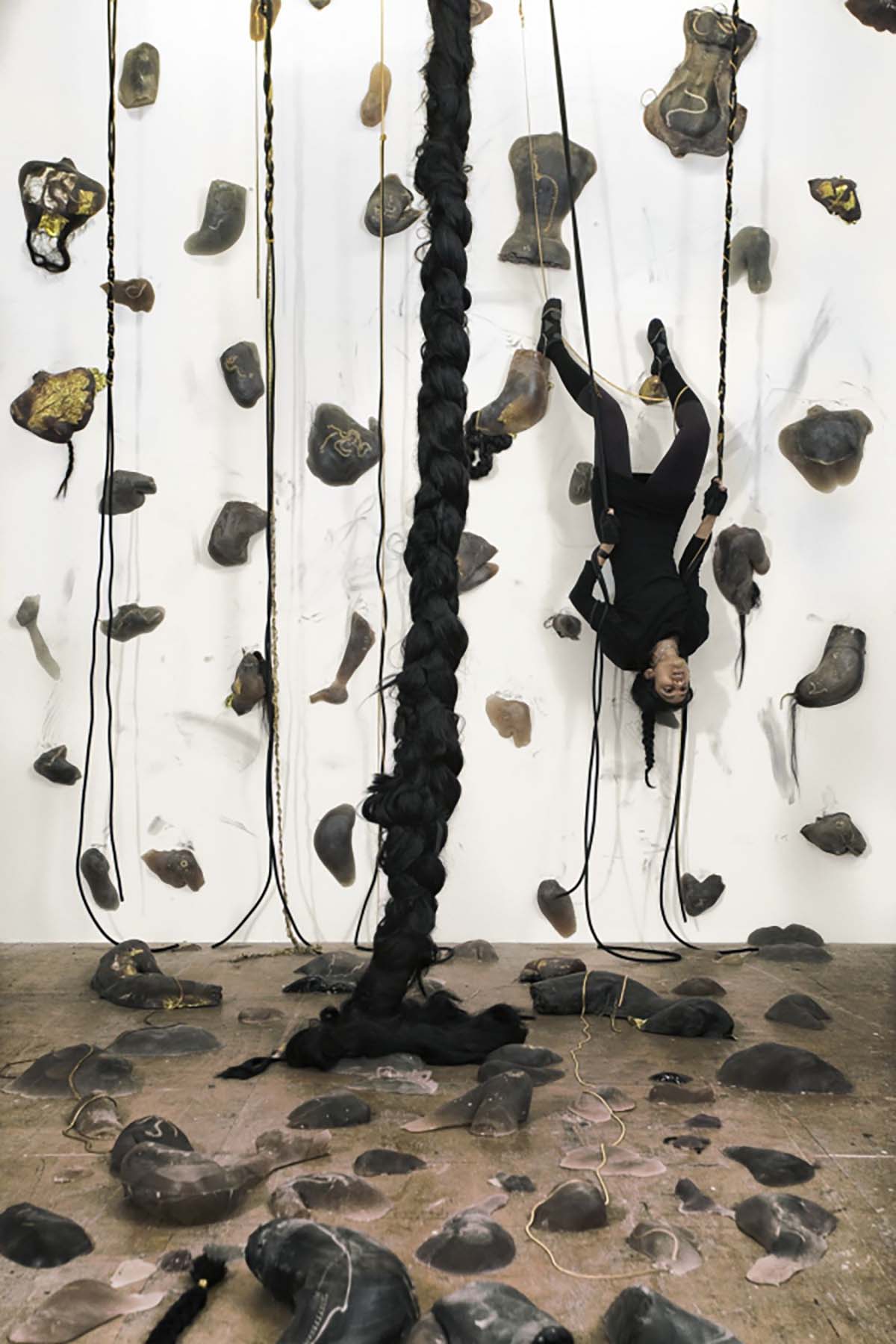 A woman hanging upside down on a rock climbing wall and a braid hanging from a ceiling