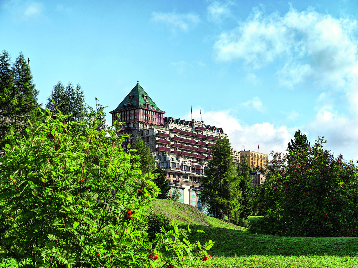 A brown grand hotel exterior with a garden in front of it 