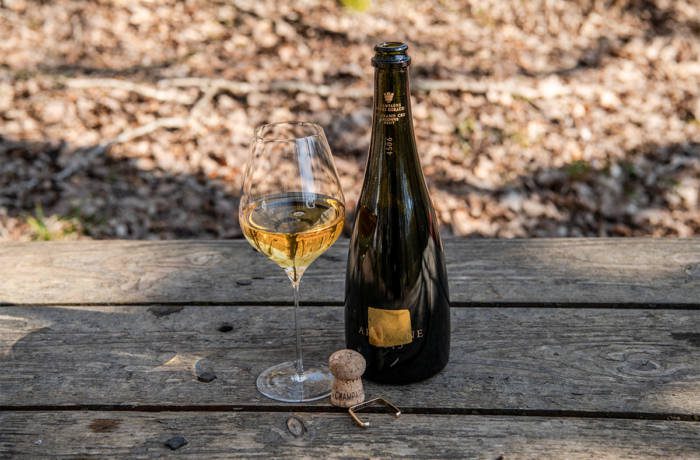 A bottle of champagne and a wine glass on a wooden table outside