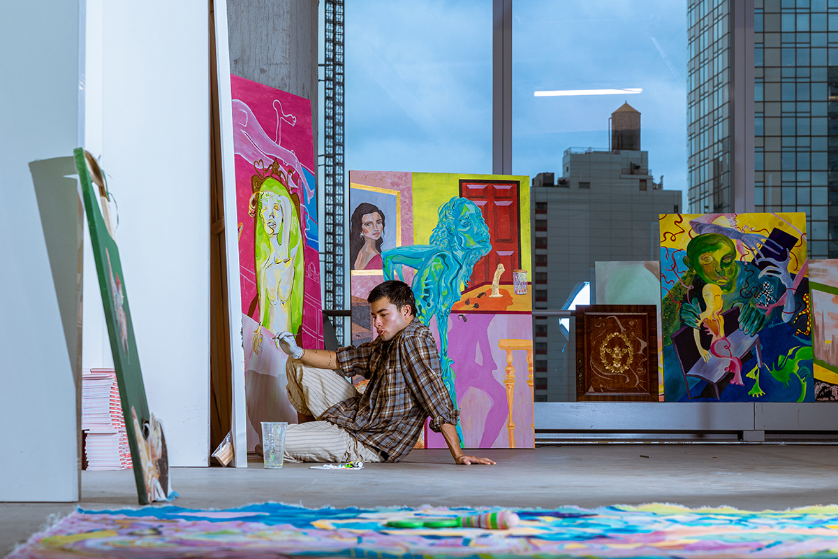 A man sitting on the floor paining on canvases with art works around him