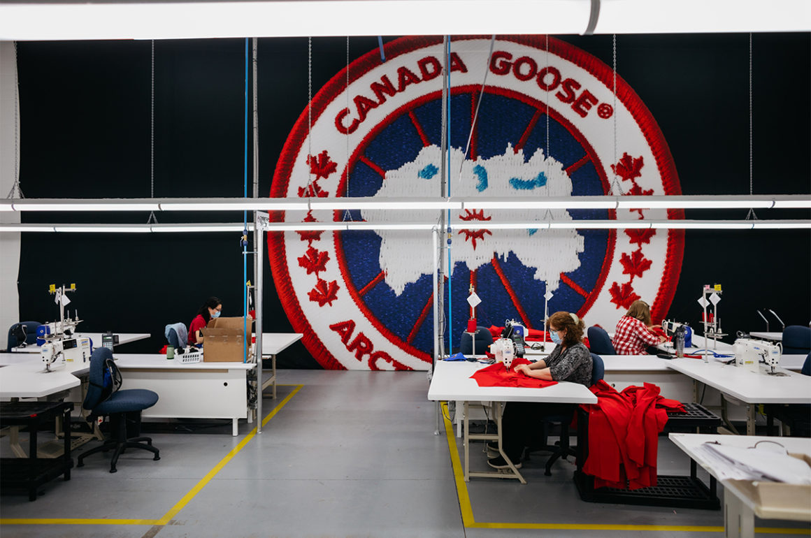 Canada Goose logo on a wall in a factory where a woman is sewing with a machine