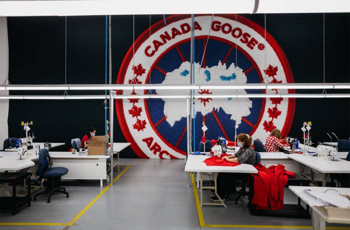 Canada Goose logo on a wall in a factory where a woman is sewing with a machine