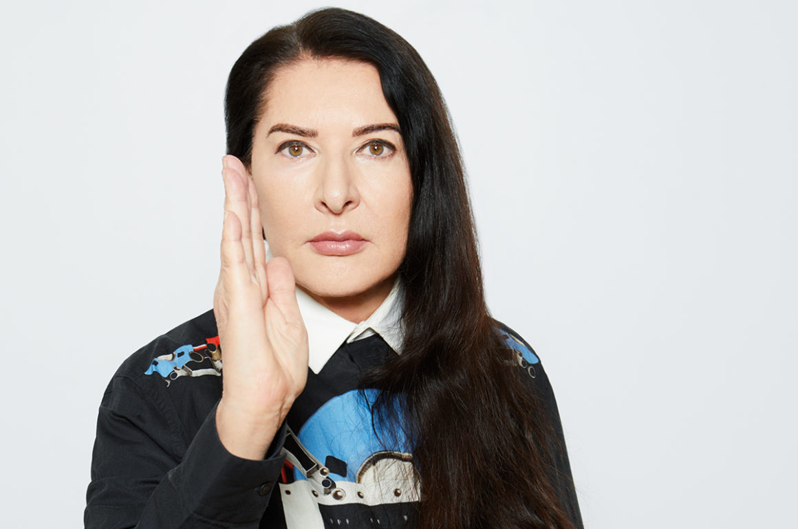 A woman with long black hair wearing a blue black and white shirt with her hand up in a karate position