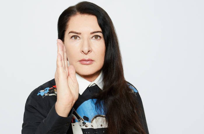 A woman with long black hair wearing a blue black and white shirt with her hand up in a karate position