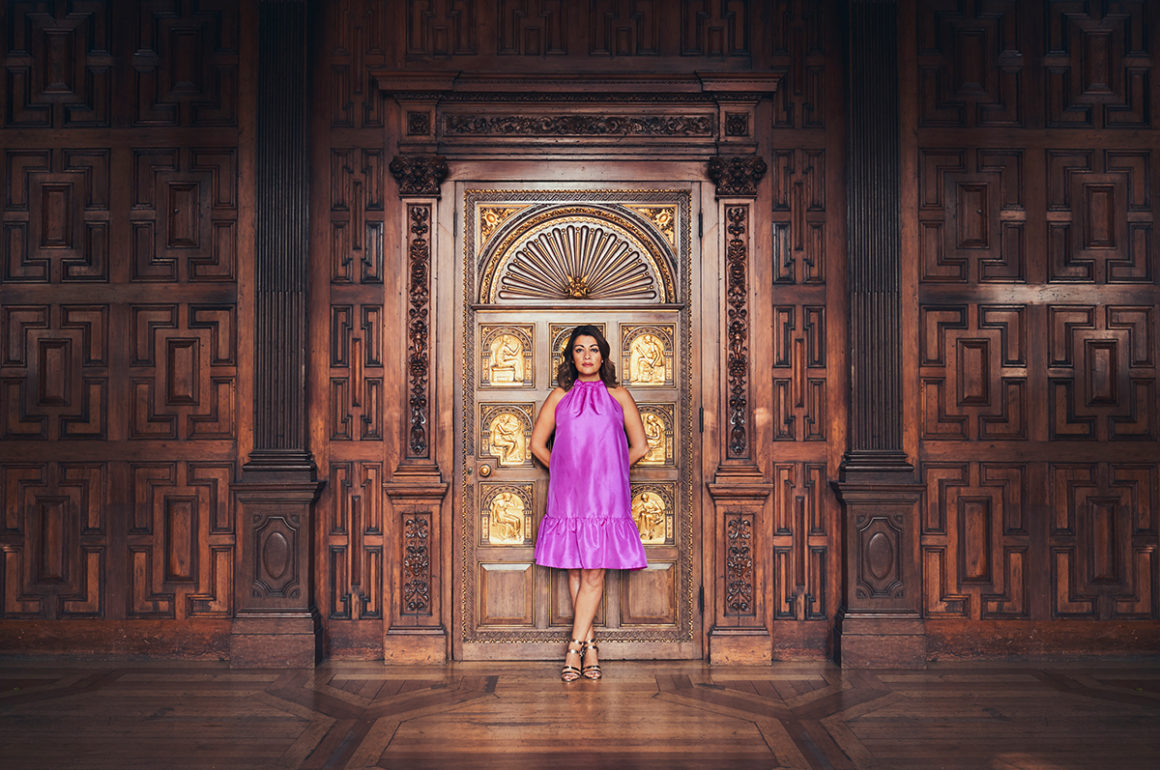 A woman in a pink dress standing in front of golden and wooden doors