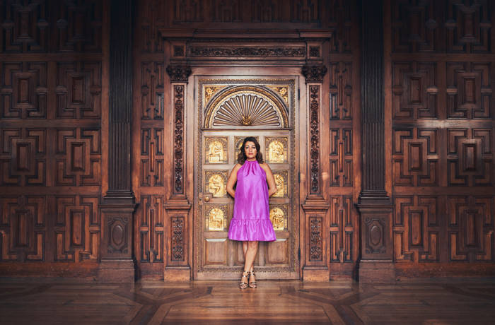 A woman in a pink dress standing in front of golden and wooden doors