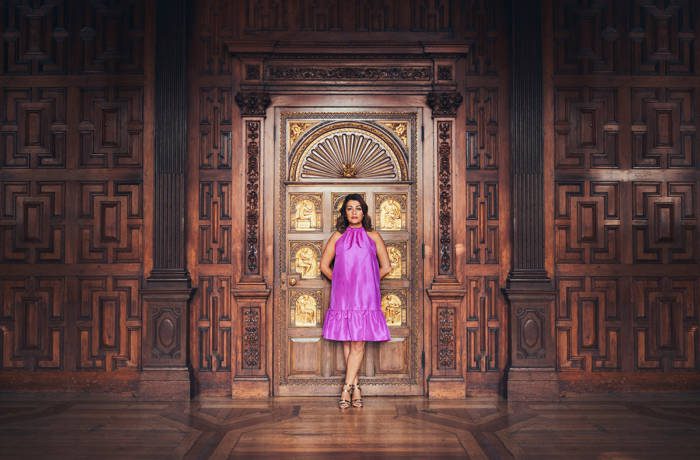 A woman in a pink dress standing in front of golden and wooden doors