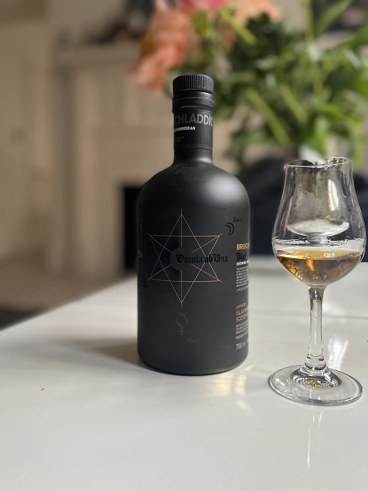 Black whiskey bottle with a star on it and a glass of whiskey on a table