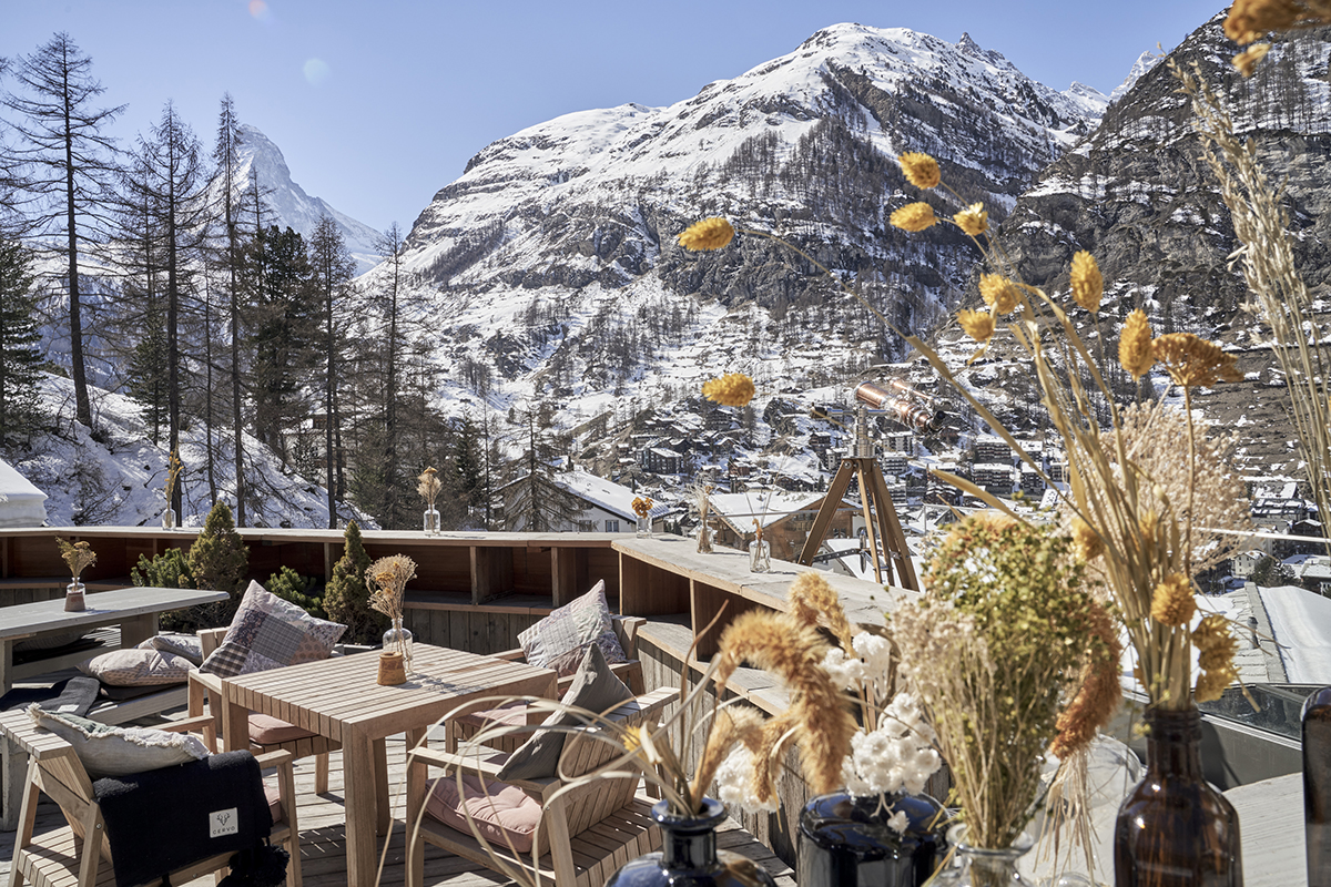 A terrace in winter with the sun and flowers and a mountain covered in snow