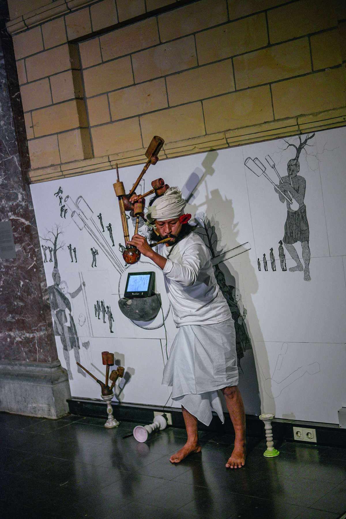 A man playing a sitar in a white outfit in front of an artwork