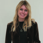 A girl with blonde hair wearing a brown jacket