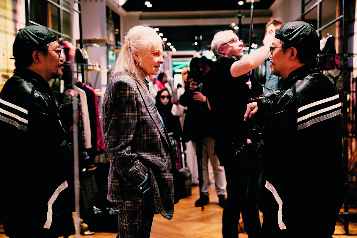 Vivienne Westwood in a grey blazer standing in a shop speaking to a man