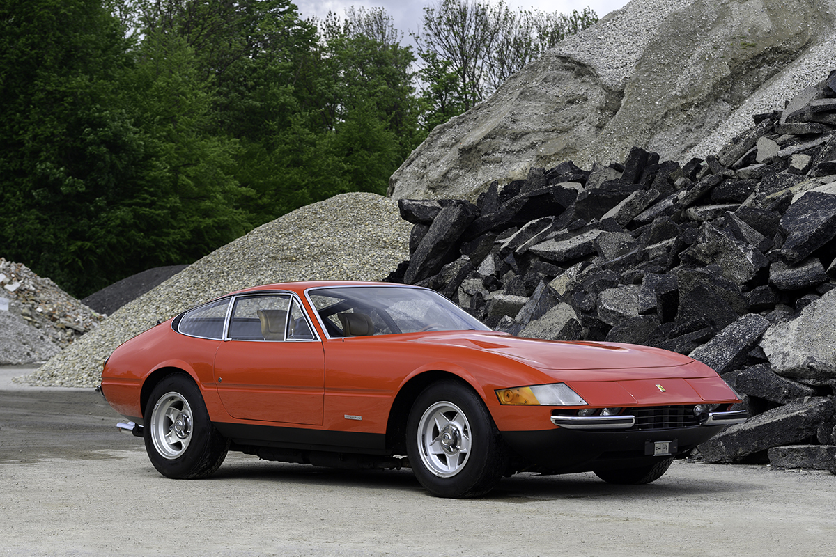 Red Ferrari on a road with stones by it